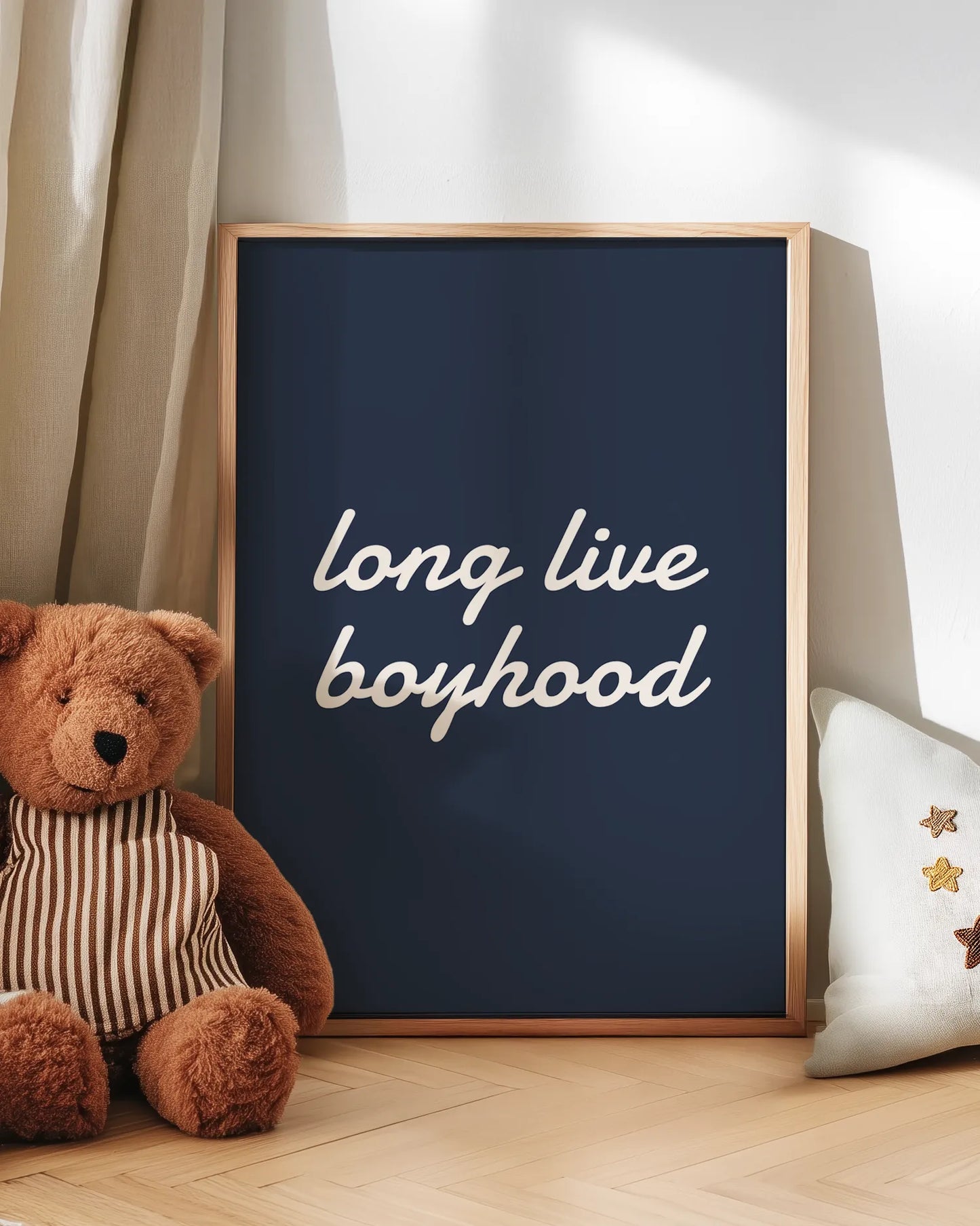 Framed artwork with 'long live boyhood' text next to a teddy bear on a wooden floor.