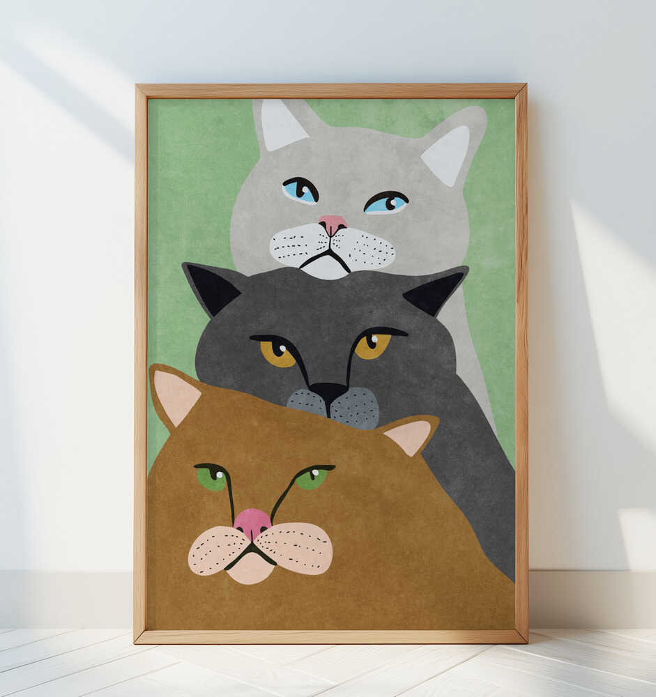 Playful cat poster with three cats stacked on top of each other, printed in earthy colors with a soft green background. The framed art print leans against a white wall, adding a modern and artistic touch to any living room or hallway decor.