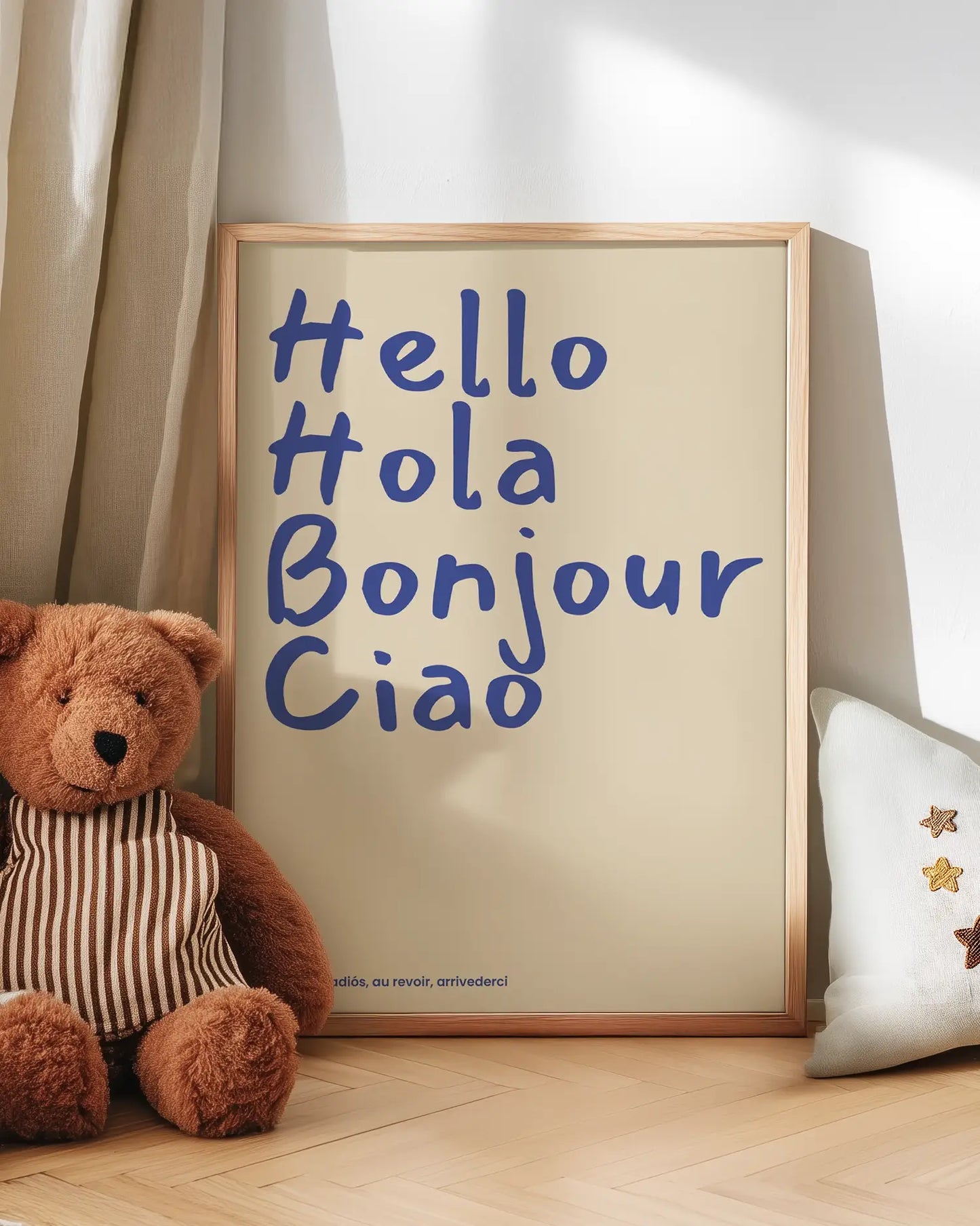 Framed picture with 'Hello Hola Bonjour Ciao' text next to a teddy bear on a wooden floor.