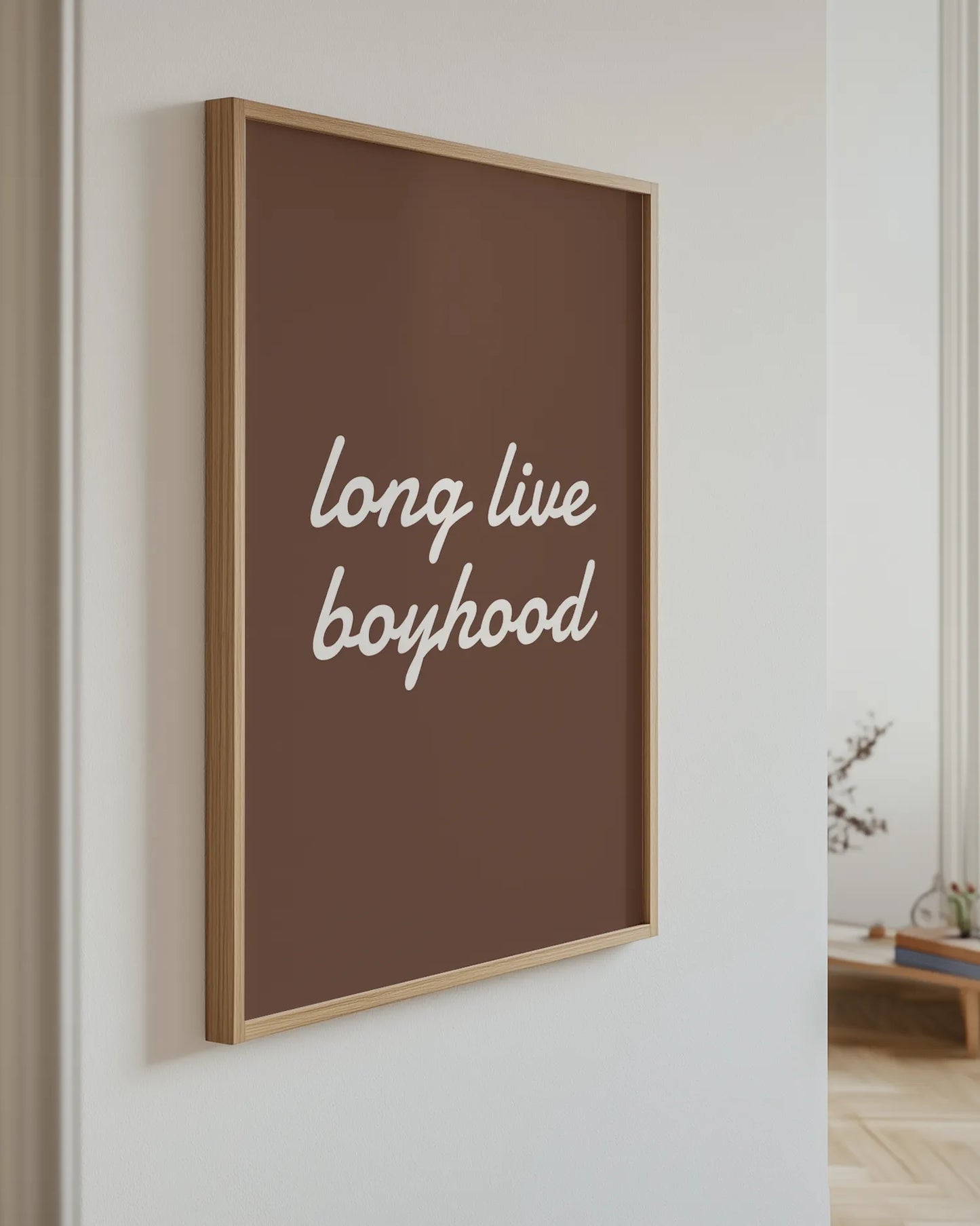 Framed artwork with 'long live boyhood' text on a brown background, hanging on a wall.